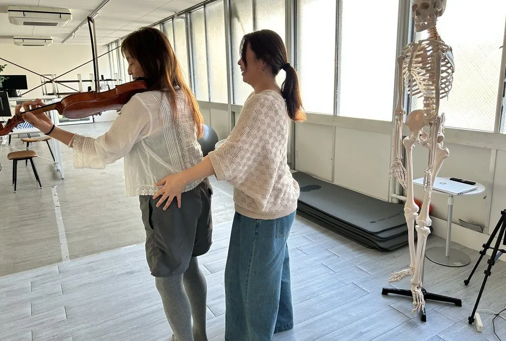 ハンズオンで骨格模型を見ながらヴァイオリンの構えを確認するレッスンの様子